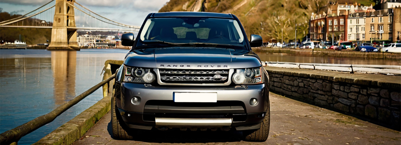 A Silver Range Rover parked on the side of a bridge with a scenic river view